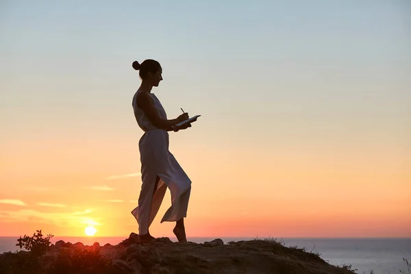 Gün batımında kişisel not defterine yazan bir kadın. Bakire doğa ve yalnız zaman fikri. Günlük ve tefekkür kavramı tutuluyor