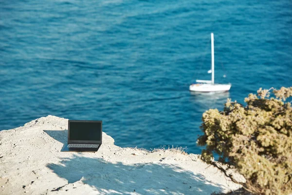 Laptop on sea rock. Sea view and yacht on background. Distance work and freelance job concept. Travelling and work idea — Stock Photo, Image