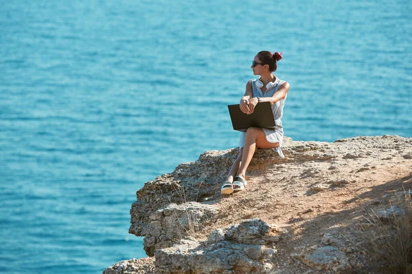 Dame assise sur la montagne regardant l'océan. Une femme travaille pendant le voyage. Temps de déplacement du bureau à distance et idée indépendante, espace de copie — Photo