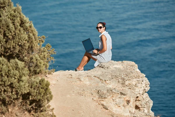 Красивая женщина работает на ноутбуке. Вид на море и девственную природу. Концепция удаленного рабочего места и времени в пути — стоковое фото