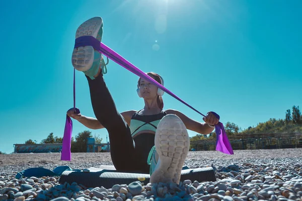 适合女人用橡皮筋伸展腿。人们在海滩上的瑜伽垫上训练。积极的生活方式和健身概念 — 图库照片