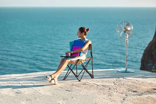 Travail à distance, concept freelance. Changement de style de vie idée. Femme souriante assise sur une chaise touristique avec des documents et un ordinateur portable — Photo