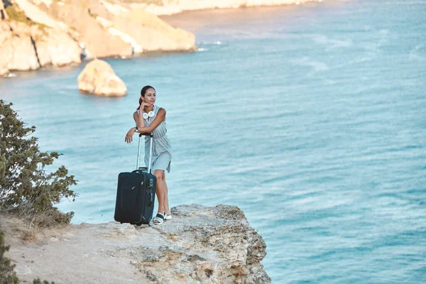 Frau mit Koffer posiert auf atemberaubender Meereslandschaft. Reise- und Sommerferienkonzept. Idee zur Änderung des Lebensstils — Stockfoto