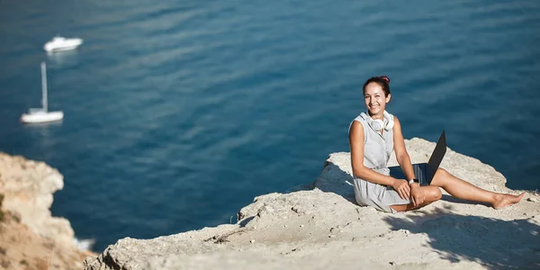 Femme souriante assise sur une haute colline avec un ordinateur portable. Travailler de n'importe où. Travail indépendant et idée de bureau à distance, espace de copie — Photo