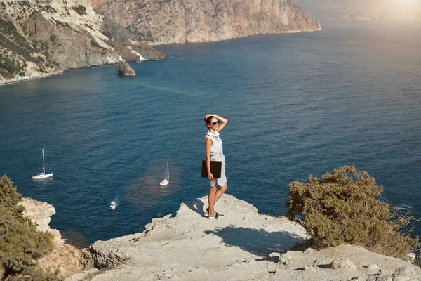 Γυναίκα που ποζάρει στον ψηλό γκρεμό και κοιτάει αλλού. Υπέροχη θέα στο βουνό και τη θάλασσα. Ελεύθερη εργασία και έννοια του απομακρυσμένου γραφείου — Φωτογραφία Αρχείου