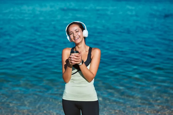 Chica feliz con taza de café escuchar música en los auriculares. Hermosa vista al mar en el fondo. Contemplación y tiempo a solas idea — Foto de Stock