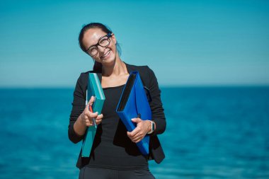 Bayan dosyalarını dokümanlarla birlikte taşıyor. Arkaplanda deniz manzarası. Yaz gezisinde çalış. Serbest meslek uzak ofis ve seyahat fikri
