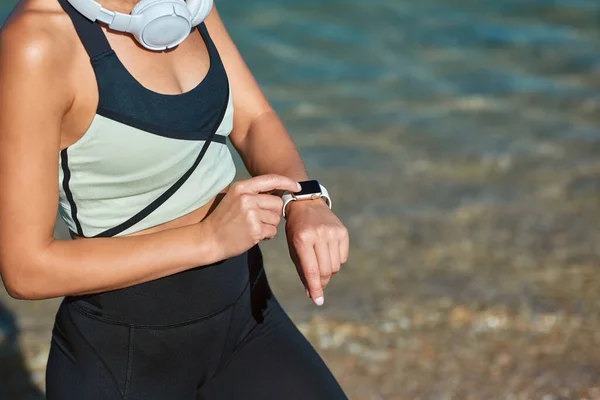 Entrenando en el aire fresco. Tiempo de deporte e idea de fitness. Hembra establece temporizador para el entrenamiento. Señora en ropa deportiva y auriculares. — Foto de Stock