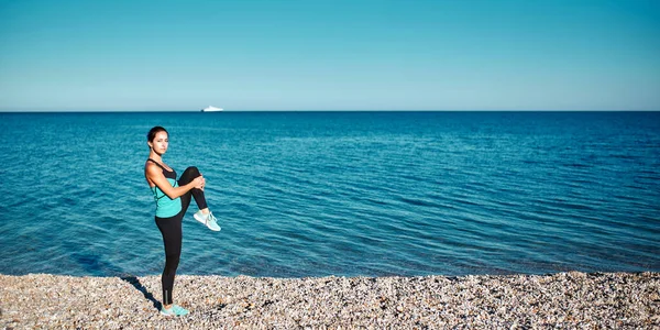 Chica calentando antes del entrenamiento. Mujer usando ropa deportiva cómoda. Calmante vista al mar. Concepto de fitness y deporte, espacio para copiar — Foto de Stock