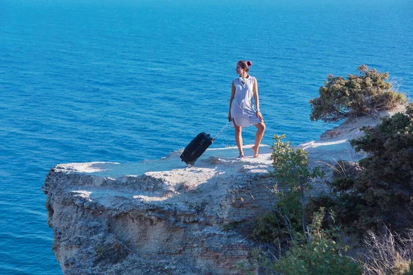 Szomjúság az utazás és az életmód megváltoztatása koncepció. Mosolygó nő bőrönddel pózol a tengeri sziklán. Tengerfenék a háttérben. — Stock Fotó