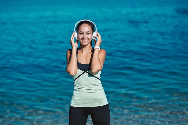 Linda dama escucha música con auriculares. Ropa deportiva con estilo para el entrenamiento. Aire fresco y naturaleza. Deporte y fitness idea — Foto de Stock
