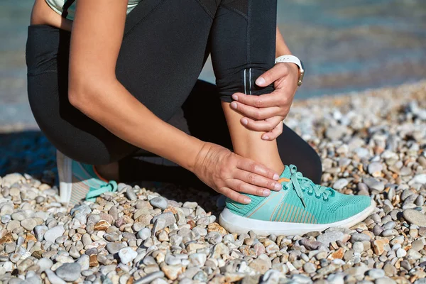 Adulto sosteniendo la pierna herida con la mano. Las mujeres se detienen en la costa rocosa. Fitness tiempo deportivo y concepto de estilo de vida saludable — Foto de Stock