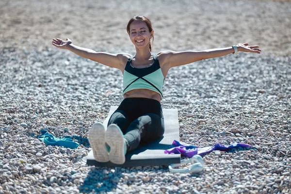 Alegre ejercicio de la mujer en la estera del yoga. Entrenamiento femenino en la costa. Deporte tiempo fitness y estilo de vida saludable concepto — Foto de Stock