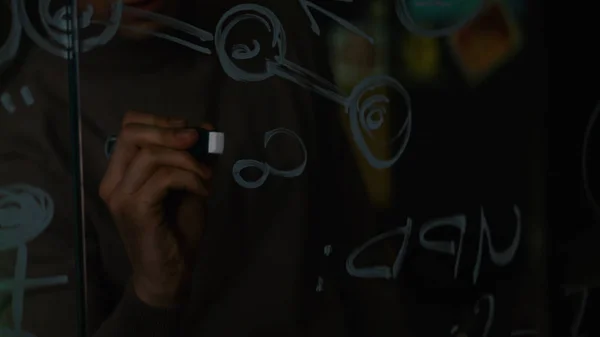 Close-up de um homem que escreve fórmulas em um quadro branco de vidro. Estoque. Close-up de um cientista escrevendo sobre a fórmula de vidro — Fotografia de Stock