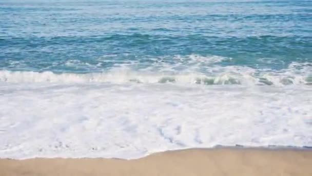 Μπλε τροπική θάλασσα με κίτρινο αμμώδη παραλία. Απόθεμα. Αμμώδης παραλία με τα κύματα της θάλασσας, σε μια ηλιόλουστη ημέρα. Καλοκαιρινό φόντο — Αρχείο Βίντεο