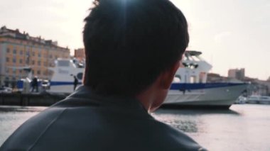 Liman kenarında oturan adam. Hisse senedi. Hipster adam günbatımında bağlantı noktası manzaraya sahiptir. Seyahat, dinlenme, tatil. Turizm kavramı