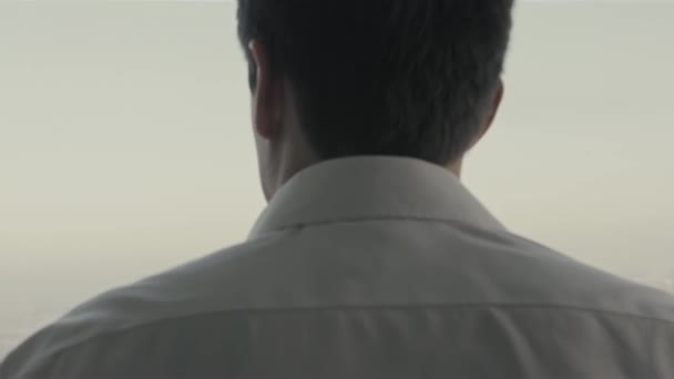 A man in a white shirt and pants is standing near a large window. Stock. Rear view of a brunet journalist stylish guy in white classic shirt — Stock Video