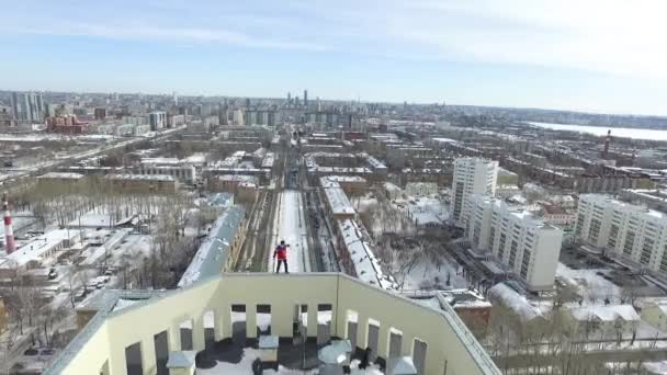 O jovem faz exercício no telhado de manhã. Vídeo. Tiro aéreo de um jovem levantado no telhado com a cidade no fundo — Vídeo de Stock