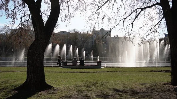 Fontein van de stad. Beeldmateriaal. Mensen lopen in het park. Fontein in stadspark op een warme zomerdag. Stroom van water, druppels en heldere spatten van water in de prachtige stad fontein — Stockfoto