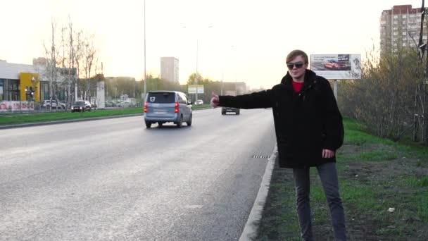 Junger Mann versucht, das Auto auf der Straße anzuhalten und hebt die Hand. Junger Mann stoppt Auto am Straßenrand — Stockvideo