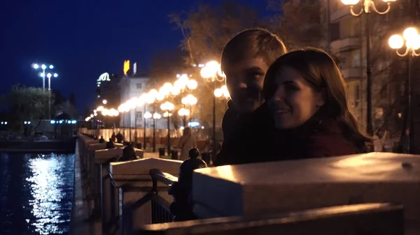 一对年轻夫妇在一条河的码头上看着一个城市。晚上在城市附近河的年轻夫妇 — 图库照片