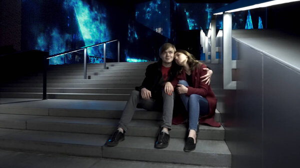 Молодая пара, сидящая на лестнице вместе на ночной улице. Целующиеся пары сидят на лестнице в центре города. Молодая пара, сидящая ночью на лестнице. Прекрасная ночь для прогулки по городу
