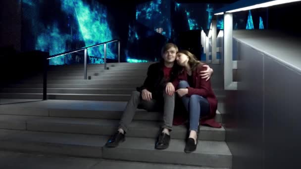 Young couple sitting on a stairs together in a night street.Kissing couple sitting on the stairs in the city center. Young couple sitting on stairs at night. Beautiful night for a walk around the city — Stock Video