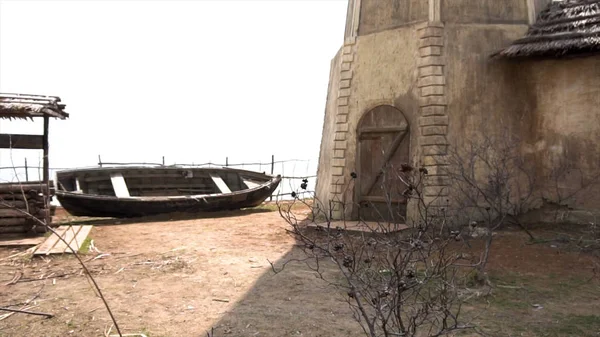 Oude vervallen zwarte houten boot met een één-verdiepingen huis, een put en een heuvel in Russische Kozak dorp. Video. Een oude boot begroeid met bloemen. Verlaten noordelijke dorp. — Stockfoto