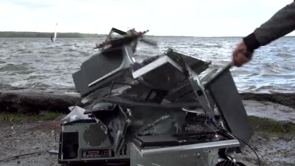 Man swings sledge hammer into printer, compuer and monitor on nature background with grasss, river, waves and sky. Concept of nature victory over technology — Stock Video