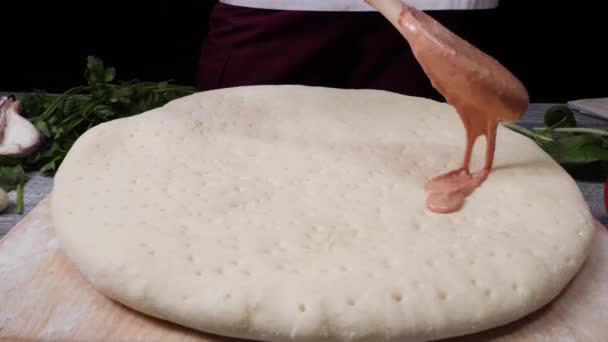 Chef cocinando pizza, preparando comida italiana tradicional con salsa marinara. Una trampa. Untar salsa de pizza en la masa — Vídeo de stock