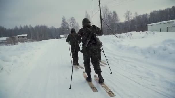 Group of soldiers run on skis in the woods with weapons. Clip. Soldiers with AK-47 rifles and grenade launchers running through the winter forest on skis. Soldiers on exercises in the woods in winter — Stock Video