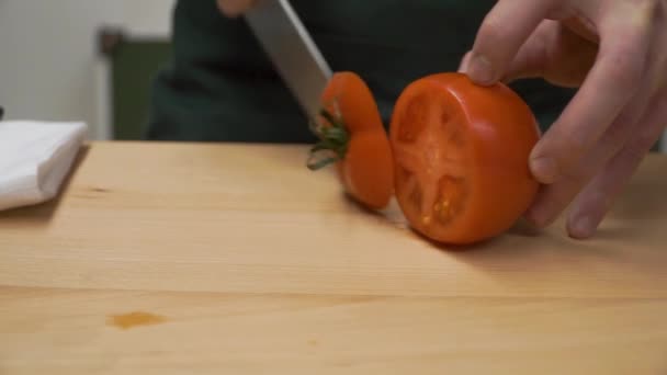 Plasterek pomidory na pół. Klip. Gotowanie, jedzenie i koncepcja domu - zbliżenie męskiej ręki pieprz cięcia na deski do krojenia w domu. zbliżenie na męskiej ręki cięcie pomidorów — Wideo stockowe