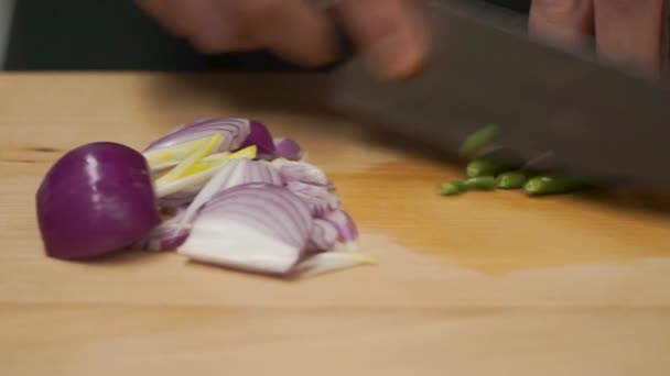 Mains masculines au couteau, coupant l'oignon frais. Clip. Découpe de repas sur une planche de bois fermer. Les mains masculines à l'aide d'un couteau coupent un oignon rouge frais sur une planche à découper. Gros plan — Video