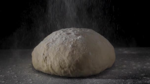 Four falling on fresh raw dough on black background in slow motion. Frame. Cook sifts the flour for the dough. Sprinkling flour over fresh dough on kitchen table. Fresh raw dough for pizza or bread — Stock Video