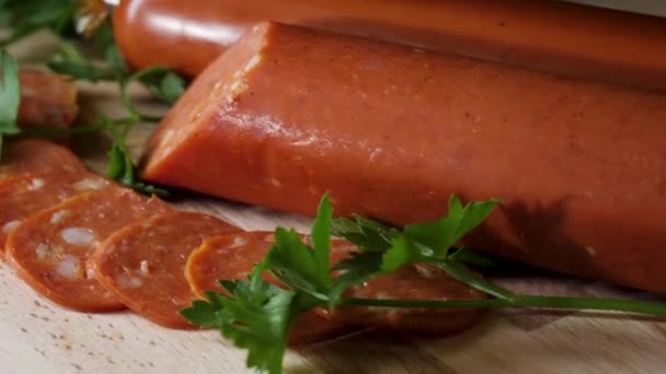 Salsicha de salame orgânica seca em tábua de corte de madeira. Moldura. Salsicha em uma tábua de madeira com alecrim e especiarias. Um pedaço de salsicha está preso no garfo. Produtos de carne alemães. Vista de cima. Rústico — Vídeo de Stock