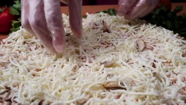 Primeros planos de cocinero panadero en uniforme blanco haciendo pizza en la cocina. Una trampa. Cocinar pizza. la pieza de trabajo sirvió salsa de tomate. Chef espolvorea pizza de queso, mucho queso en una pizza, proceso de cocción — Vídeos de Stock