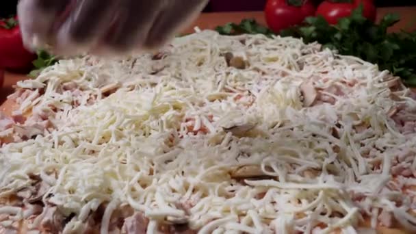 Primeros planos de cocinero panadero en uniforme blanco haciendo pizza en la cocina. Una trampa. Cocinar pizza. la pieza de trabajo sirvió salsa de tomate. Chef espolvorea pizza de queso, mucho queso en una pizza, proceso de cocción — Vídeo de stock