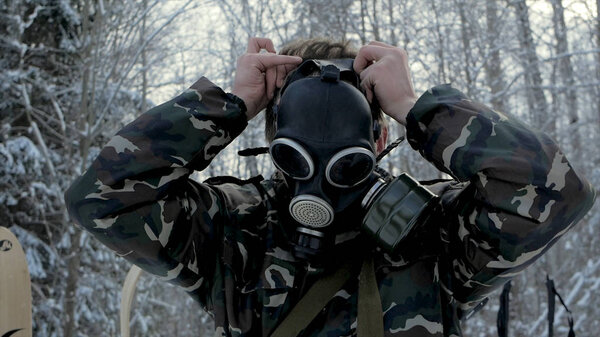 Man in uniform wearing a gas mask in the winter forest. portrait of a young soldier wearing a gas mask against a nature background.