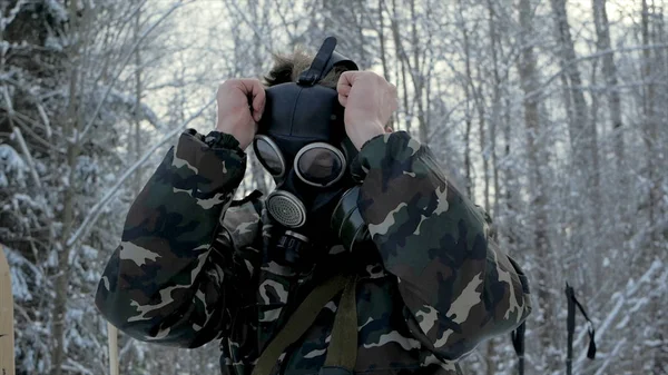 冬の森でガスマスクを身に着けている制服を着た男。自然を背景にガスマスクを身に着けている若い兵士の肖像画. — ストック写真