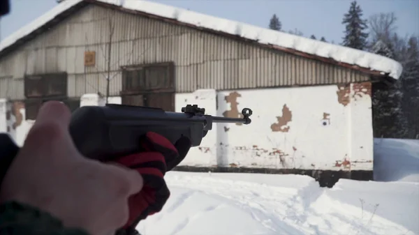 Um homem apontando uma pistola de pellet em direção a um alvo, praticando seu objetivo no inverno. Clipe. O atirador em camuflagem tem como alvo um alvo com uma espingarda com visão óptica, focado em armas . — Fotografia de Stock