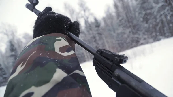 Un hombre apuntando una pistola de perdigones hacia un objetivo, practicando su puntería en invierno. Clip. El tirador en camuflaje apunta a un objetivo con un rifle con una vista óptica, se centran en las armas . — Foto de Stock