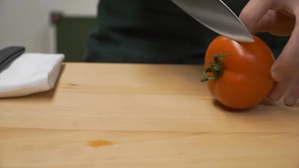 Skiva tomaterna i hälften. Klipp. Matlagning, mat och hem concept - Närbild manlig hand skära peppar på skärbrädan hemma. närbild på manlig hand skära tomat — Stockfoto