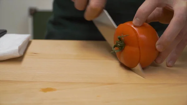 Tagliare i pomodori a metà. Clip. cottura, cibo e concetto di casa - primo piano di maschio mano tagliando pepe sul tagliere a casa. primo piano del pomodoro maschio tagliato a mano — Foto Stock