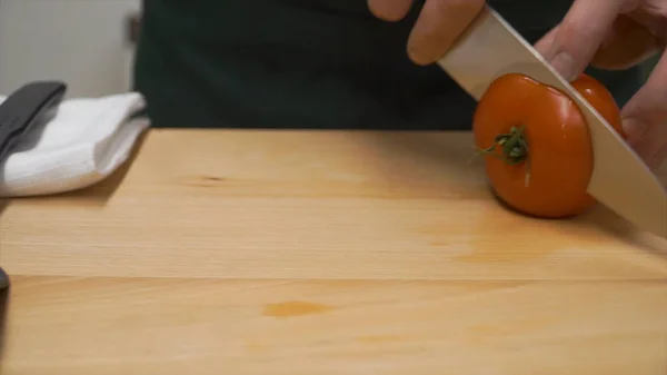 Tagliare i pomodori a metà. Clip. cottura, cibo e concetto di casa - primo piano di maschio mano tagliando pepe sul tagliere a casa. primo piano del pomodoro maschio tagliato a mano — Foto Stock