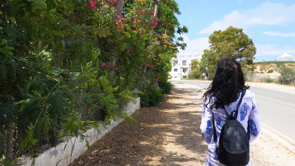 Woman walking along road in tropics. Beautiful woman traveler walking along the road, back view