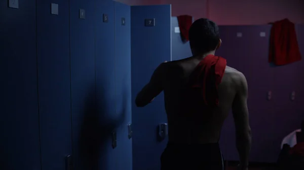 Disappointed and tired sportsman in semi lit locker room. Sad athlete in the locker room after the defeat at the tournament