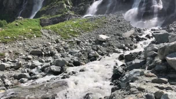 Hegyi vízesést. Vízfolyások elesik a sziklák a napsütésben. Rohanó víz a lassú mozgás. Fröccsenő víz, zöld fű — Stock videók