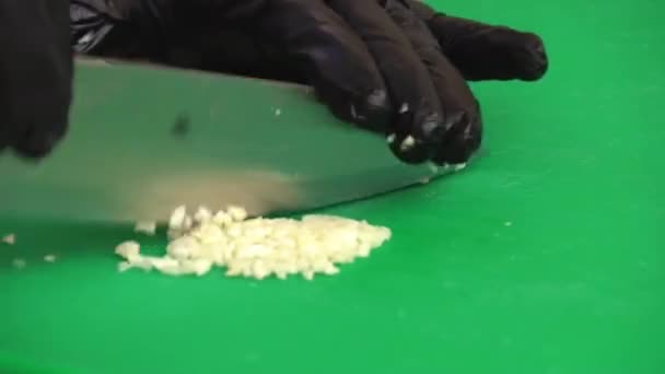 Крупним планом професійні кухарські руки використовують ніж для дрібно нарізання скибочки часнику для приготування їжі — стокове відео