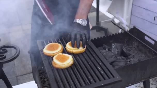 Man making burger. chef in form and gloves cooking sandwiches. Summer picnic. Chef with gloves roasting buns for hamburgers — Stock Video