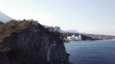 Havadan görünümü ile orman ve dağlar arka plan ve mavi gökyüzü ile lüks otel sahil üzerinde. Video. Beyaz lüks otelin dağlar, orman ve gökyüzü ile kıyı şeridi denizde güzel yaz üstten görünüm